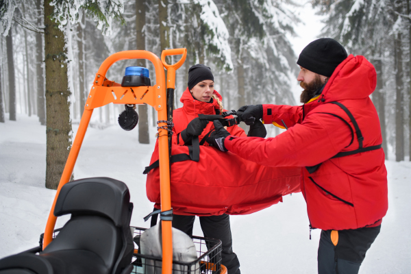 Paramedic woman from mountain rescue service provide an operation outdoors in winter in forest.