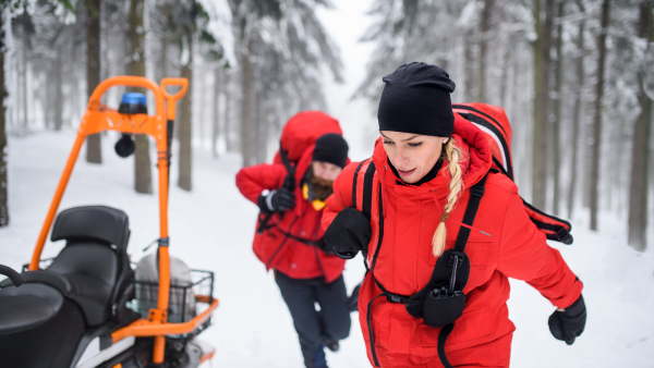 Paramedics from mountain rescue service provide operation outdoors in winter in forest, walking.