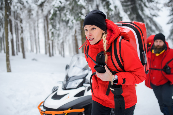 Paramedics from mountain rescue service provide operation outdoors in winter in forest, walking.