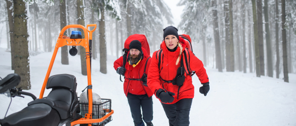 Paramedics from mountain rescue service provide operation outdoors in winter in forest, walking.