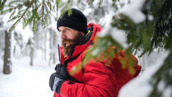 Paramedic man from mountain rescue service with walkie talkie outdoors in a winter in forest.