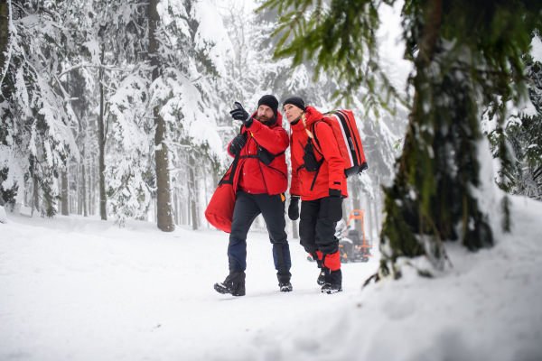 Paramedics from mountain rescue service walking and talking outdoors in winter in forest.