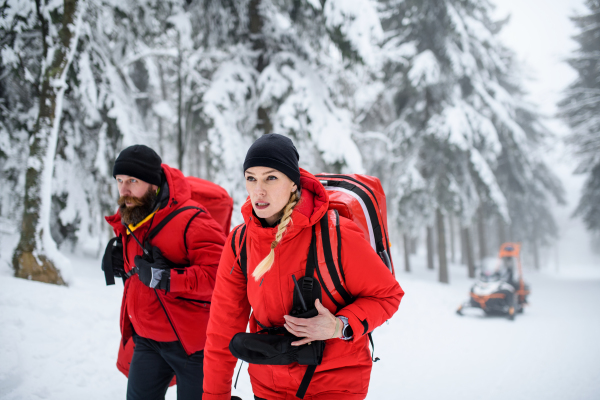 Paramedics from mountain rescue service walking and talking outdoors in winter in forest.