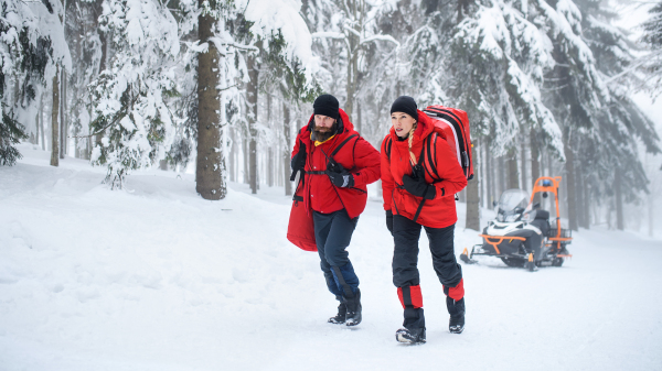 Paramedics from mountain rescue service walking and talking outdoors in winter in forest.