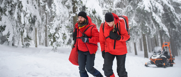 Paramedics from a mountain rescue service walking outdoors in winter in forest.