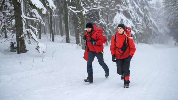 Man and woman paramedics from mountain rescue service running outdoors in winter in forest.