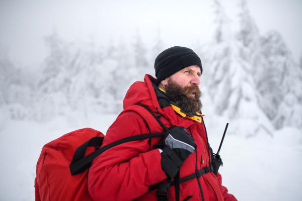 Paramedic man from mountain rescue service with walkie talkie outdoors in a winter in forest.