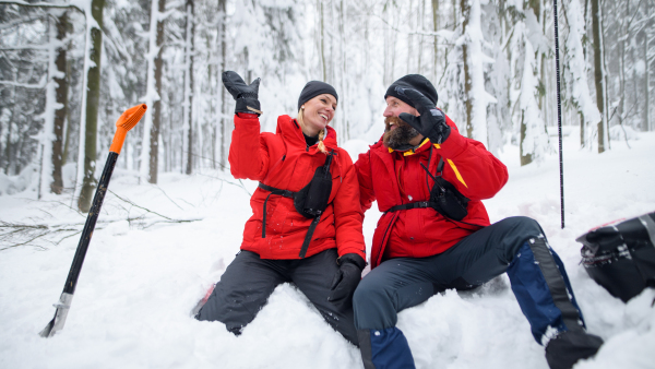 Mountain rescue service on operation outdoors in winter in forest, digging snow with shovels and giving figh five.