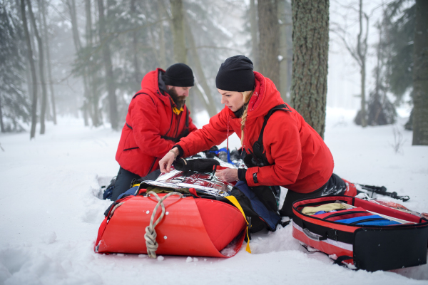 Paramedics from mountain rescue service provide operation outdoors in winter in forest, injured person in stretcher.