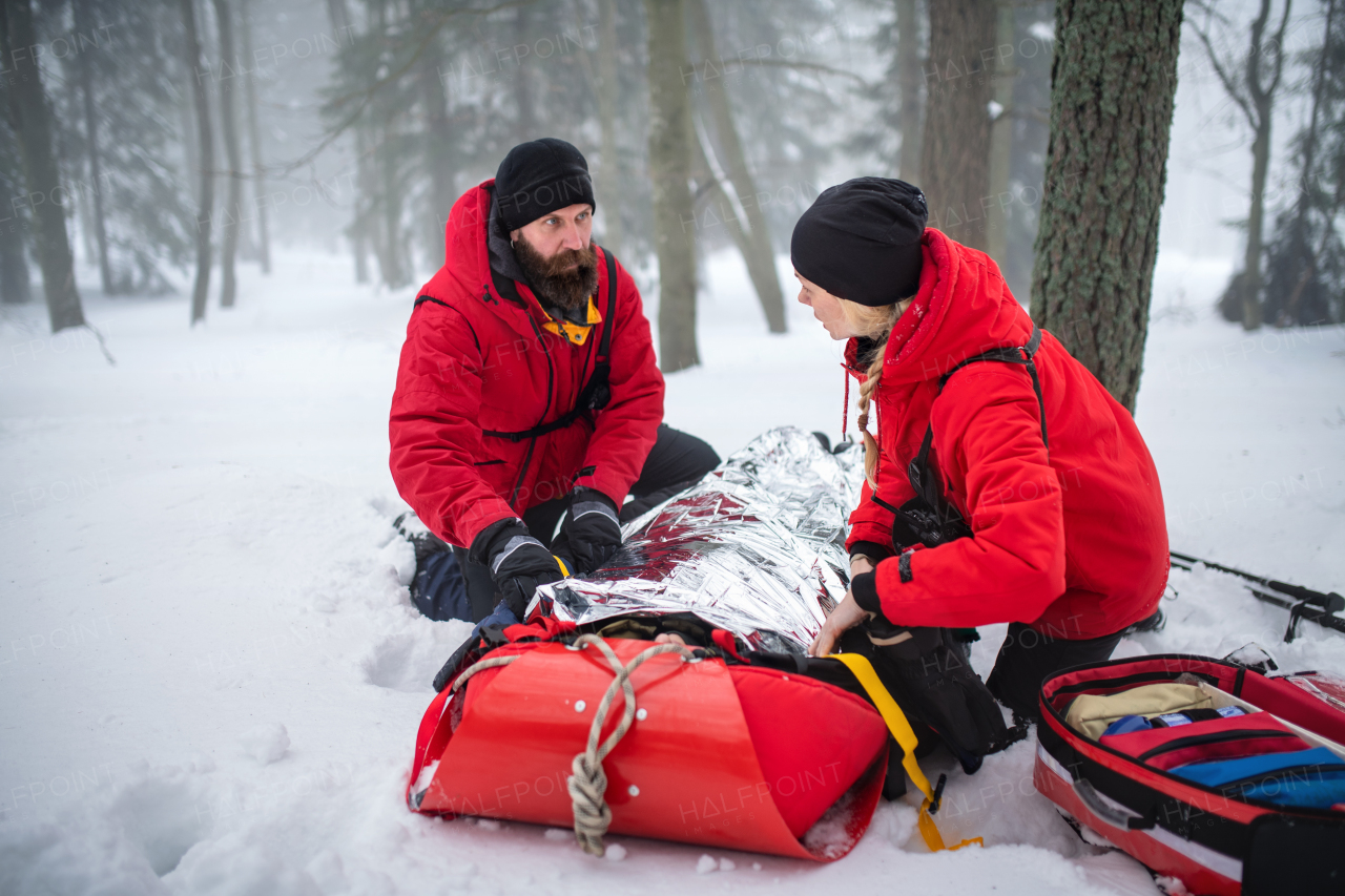 Paramedics from mountain rescue service provide operation outdoors in winter in forest, injured person in stretcher.