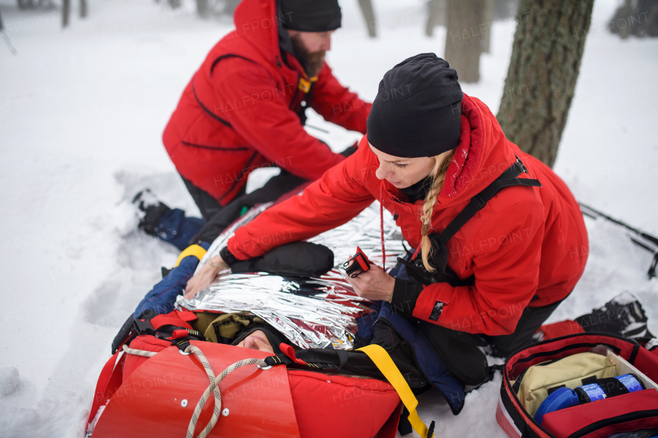 Paramedics from mountain rescue service provide operation outdoors in winter in forest, injured person in stretcher.