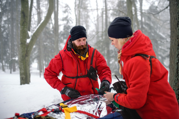 Paramedics from mountain rescue service provide operation outdoors in winter in forest, injured person in stretcher.