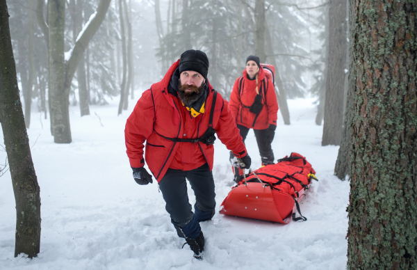 Paramedics from mountain rescue service provide operation outdoors in winter in forest, injured person in stretcher.