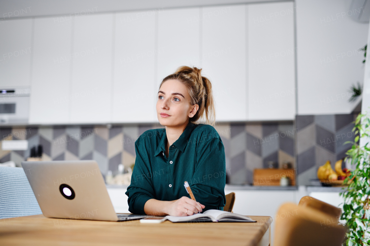 A young woman student with laptop writing notes at home, home office and learning.