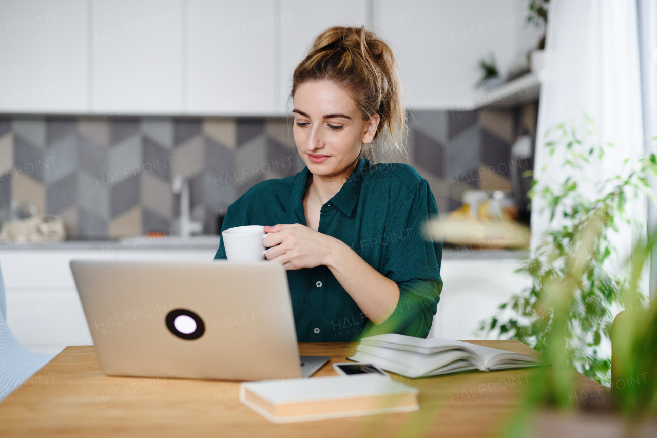 A young woman student with laptop writing notes at home, home office and learning.