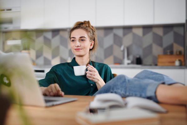 A young woman student with laptop writing notes at home, home office and learning.