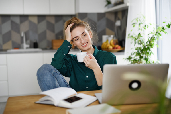 A young woman student with laptop drinking coffee, home office and learning.