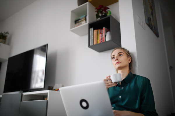 A young woman student with laptop daydreaming at home, home office and learning.