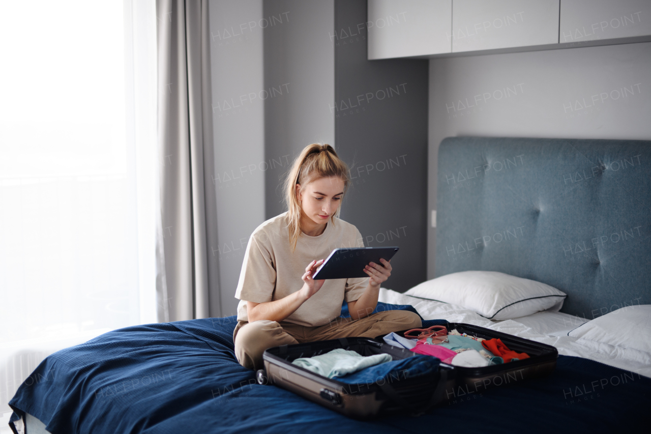 A portrait of young woman sitting on bed indoors at home, planning holiday.