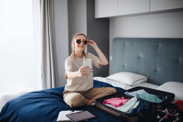 A portrait of young woman taking selfie indoors at home, planning holiday.