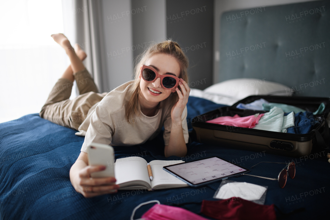 A portrait of young woman taking selfie indoors at home, planning holiday.