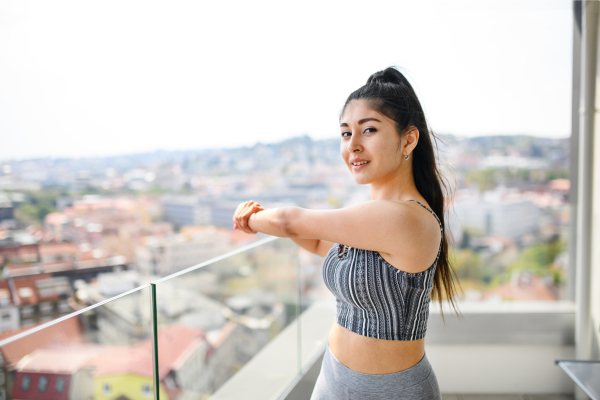 A portrait of young sport woman doing exercise on balcony outdoors in city, looking at camera.