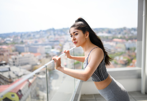 A portrait of young sport woman doing exercise on balcony outdoors in city, stretching.