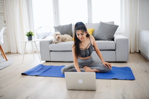 A portrait of young sport woman with laptop doing exercise indoors at home, healthy lifestyle concept.