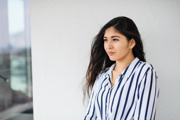 A portrait of young woman standing against white background, looking aside.