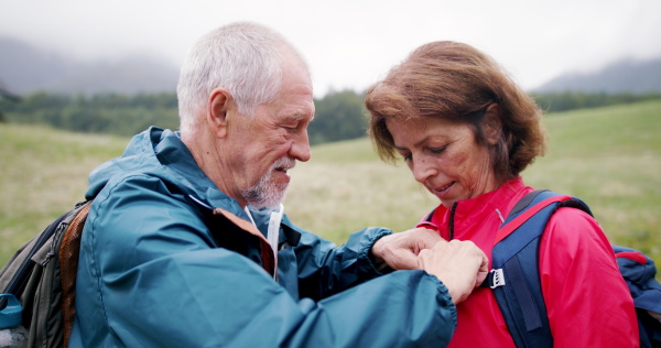 Front view of happy senior pensioner couple hiking in nature, advancing backpack.