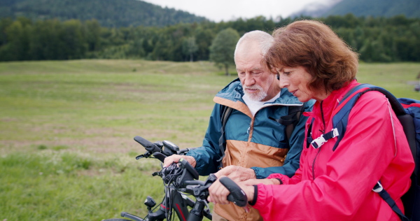 Senior pensioner couple bikers with bicycles talking in nature, cycling trip concept.