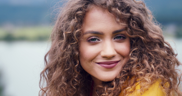 Close-up portrait of young woman tourist on a hiking trip in nature, standing and looking at camera.