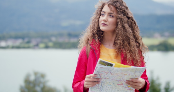 Happy young woman tourist with a backpack on a hiking trip in nature, standing with map.