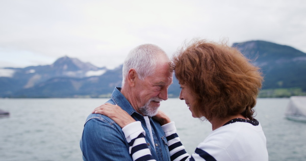 Side view of senior pensioner couple tourists cuddling on pier by big lake.