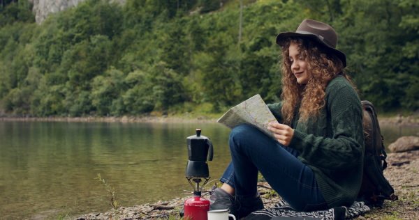 Young woman tourist with a map on a hiking trip in nature, sitting and resting.