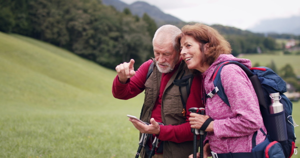 A senior pensioner couple hiking in nature, using smartphone.