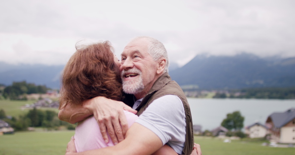 A senior pensioner couple hiking in nature, hugging.