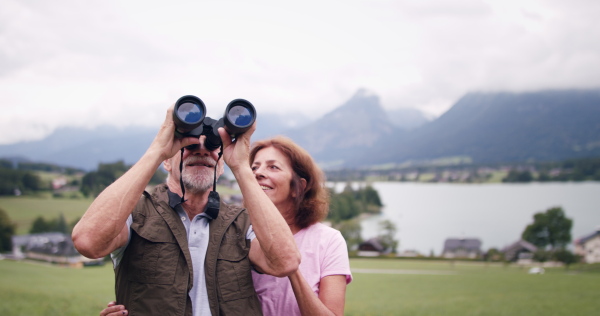 Portrait of senior pensioner couple with binoculars hiking, resting and talking.