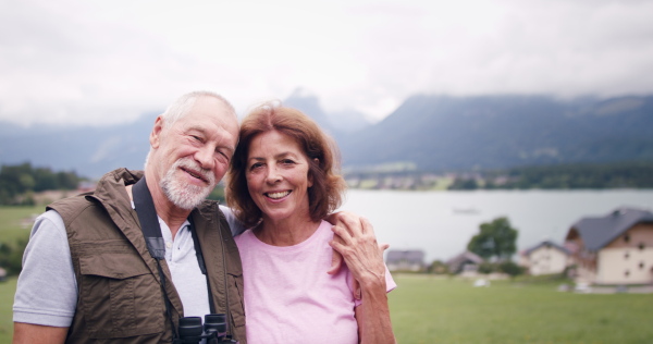 A senior pensioner couple hiking in nature, looking at camera.