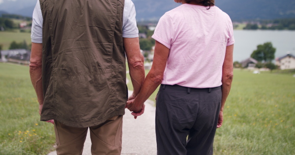 A rear view of active senior pensioner couple hiking in nature, holding hands. Close up on hands.