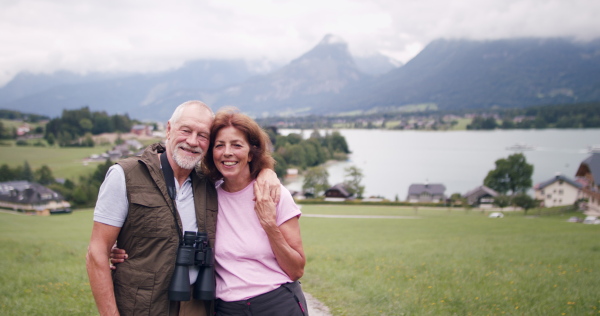 An active senior pensioner couple hiking in nature, hugging.