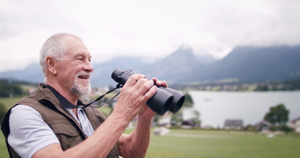 A senior pensioner hiking in nature, using binoculars.