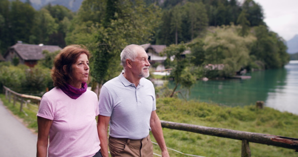 Happy senior pensioner couple by lake hiking in nature, talking.