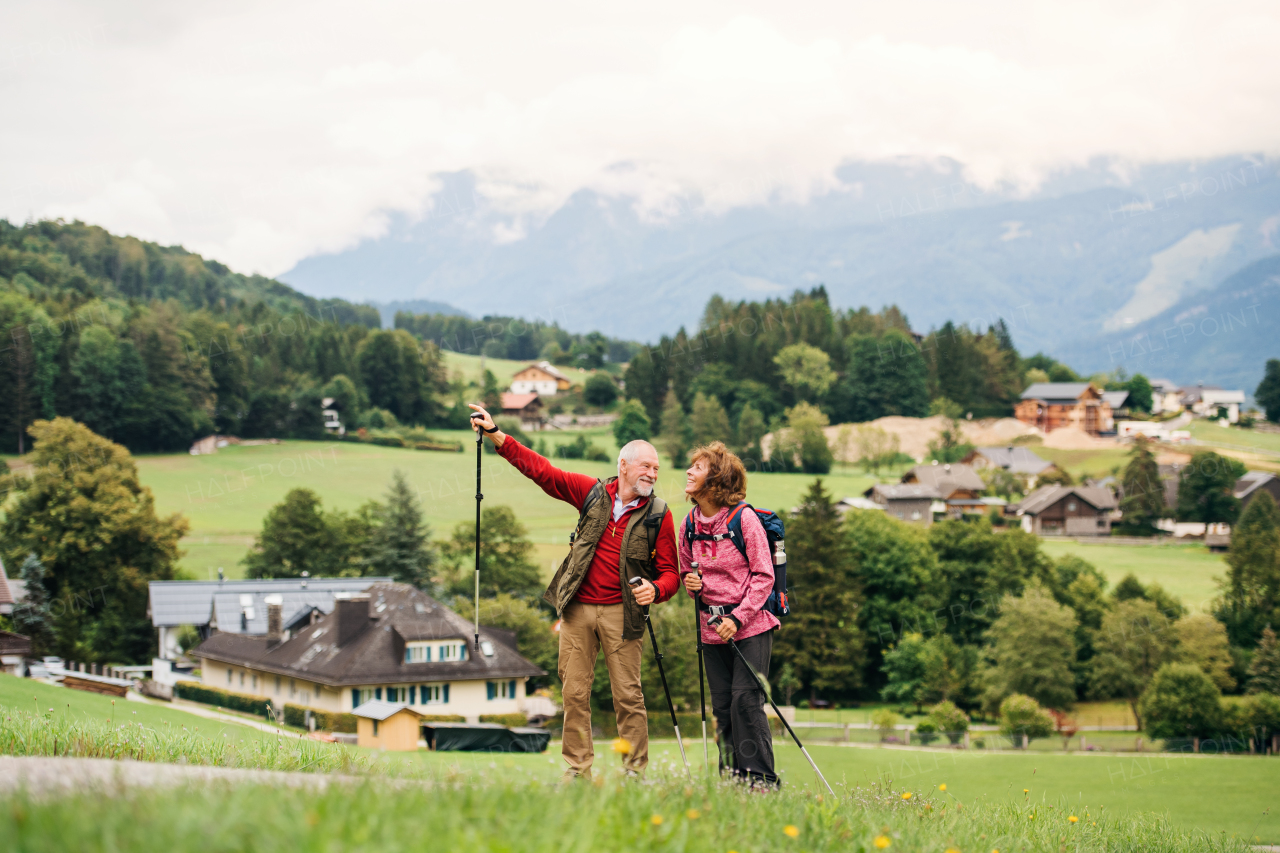 A senior pensioner couple with nordic walking poles hiking in nature, talking.