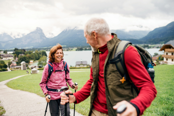 A senior pensioner couple with nordic walking poles hiking in nature, talking.