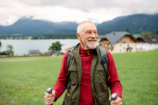 A senior man with nordic walking poles hiking in nature, resting.