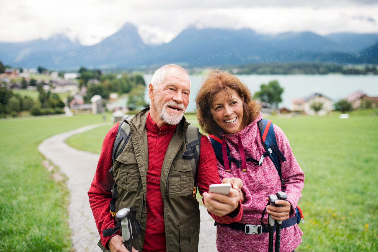 A senior pensioner couple with hiking in nature, using smartphone.