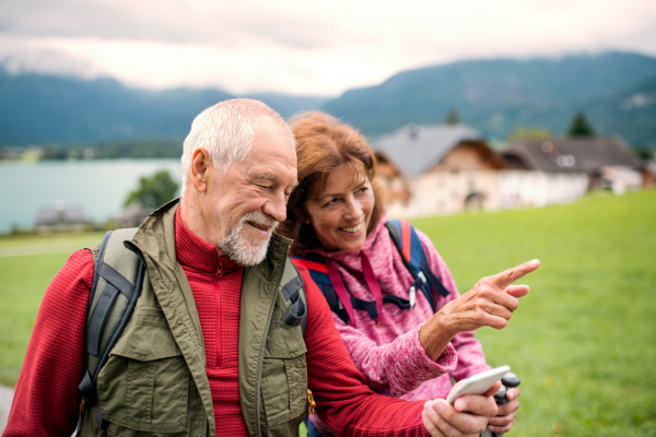 A senior pensioner couple hiking in nature, using smartphone.