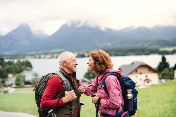 A senior pensioner couple with nordic walking poles hiking in nature, talking.