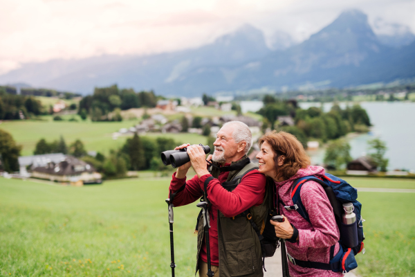 A senior pensioner couple with hiking in nature, using binoculars.